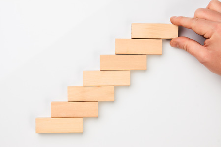Man hand put wooden blocks in the shape of a staircase isolated on white background with copy space. Concept of building success foundationの写真素材