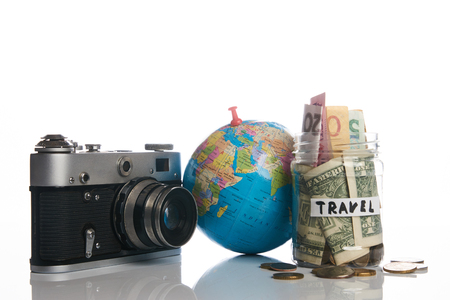 Travel budget concept. Travel money savings in a glass jar with photo camera and globe on a white background, close-up.の写真素材