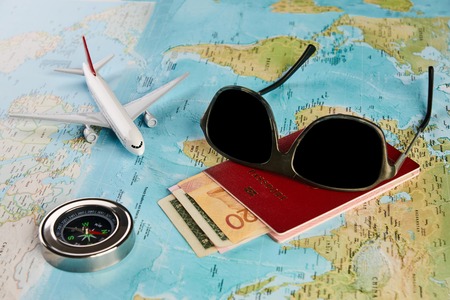 Vacation holidays travel concept with sunglasses compass navigation, passport travel document with money and aircraft on a world map, close-upの写真素材