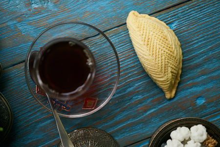 Traditional Azerbaijan sweet pastry shekerbura with nuts and honey and glass of black tea on wooden table background, close up. Delicious dessert Shekerbura baked during the spring holiday Novruz.の写真素材