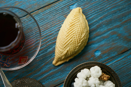 Traditional Azerbaijan sweet pastry shekerbura with nuts and honey and glass of black tea on wooden table background, close up. Delicious dessert Shekerbura baked during the spring holiday Novruz.の写真素材