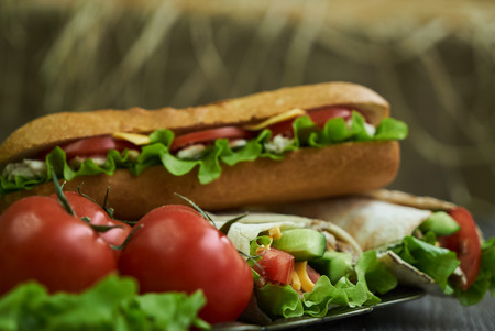 Shaurma chicken roll in a pita with fresh vegetables and long subway sandwich with tomatoes, cucumber, latitude, cheese and chicken breast fillet meat on wooden table, close-upの写真素材