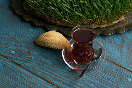 Glass of tea with Azerbaijan pastry shekerbura and wheat grass semeni on blue wooden table background. Novruz holiday foodの写真素材