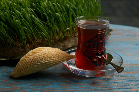 National Azerbaijan pastry shekerbura with nuts and honey and glass of black tea on wooden table with wheat grass semeni,background, close up. Novruz holiday dessertの写真素材