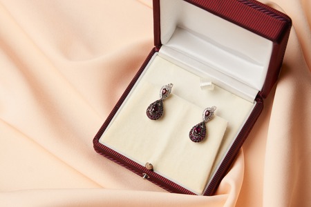 Pair of ruby diamond earrings with red ruby stone on a silk peach background. Luxury female jewelry in present gift box, close-upの写真素材