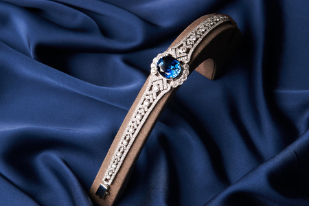 Beautiful platinum bracelet. Luxury women bracelet with diamonds and sapphire on blue silk background, close-upの写真素材