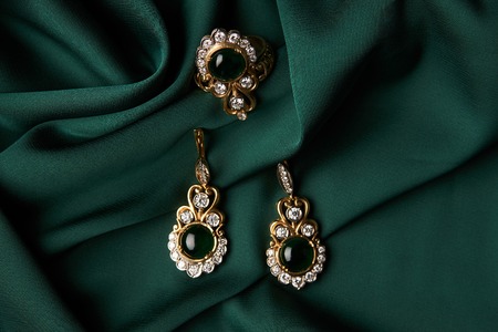Diamond ring and earrings with emerald on a green silk background. Luxury female jewelry, close-up