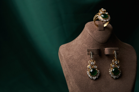 Diamond ring and earrings with emerald on a green silk background. Luxury female jewelry, close-upの写真素材