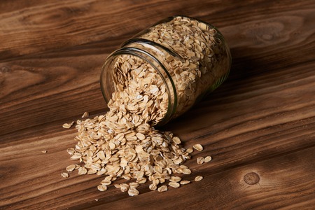 Oatmeal glass jar on wooden background. Glass jar with oatmeal flakes, close-up. Scattered oat. Dry,...