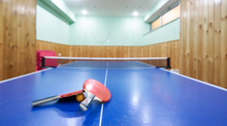 Blurred table tennis table, rackets and balls in a sport hall.