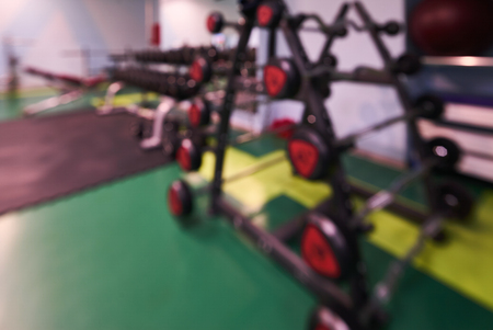 Blurred interior of fitness center. Sport exercise equipment for bodybuilding weight and dumbbells...
