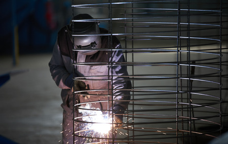 Welder man in welding mask welds at the factory
