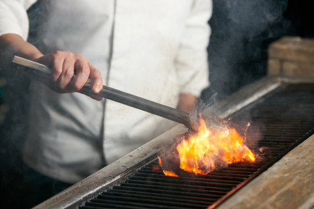 Chef grilling beef steak on flame on bbq in the kitchen of restaurant, close-upの写真素材