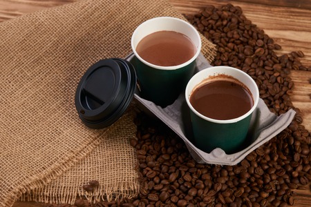 Close-up of three take away green paper cups in coffee holder container with coffee beans and hot chocolate drink on rustic wooden table background, top view,の写真素材