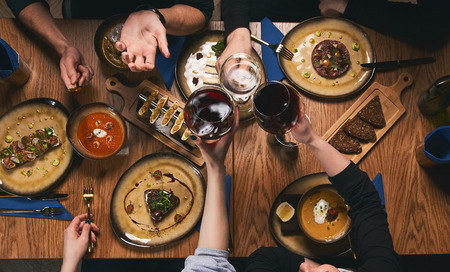 Table with food, top view. Flat-lay of friends hands eating and drinking together. People having...