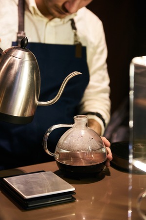 Professional barista pouring hot water on coffee glassware . Drip coffee or pour-over coffee on the...