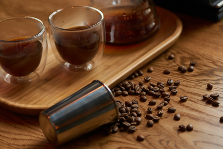 Coffee beans, metal cup and glass cup of coffee drink on wooden table background, close-up.
