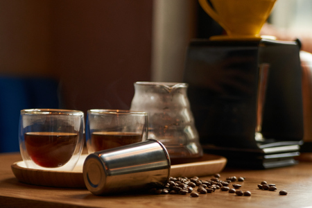 Coffee beans, metal cup and glass cup of coffee drink on wooden table background, close-up.の写真素材