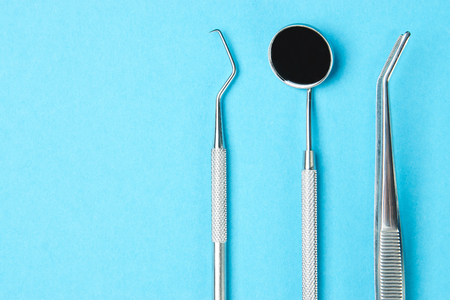 Professional Dentist tools on blue background with copy space. Dentist mirror, forceps curved, explorer curved, dental explorer angular and explorer curved with chip in dental office. Hygiene conceptの写真素材