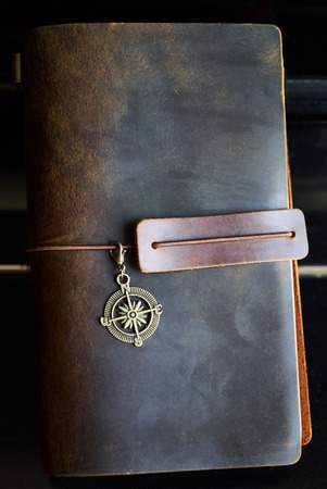 Travel note on black background. Handmade paper diary notebook in brown leather cover. Old vintage leather book, top view.の写真素材
