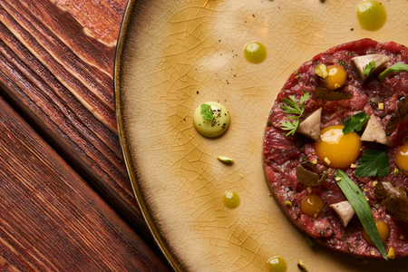 Tartare Steak with egg yolk, pistachios, truffle oil, green mayonnaise on plate and glass of red wine, served on restaurant table. Classic Beef tartare meat, Luxury foodの写真素材
