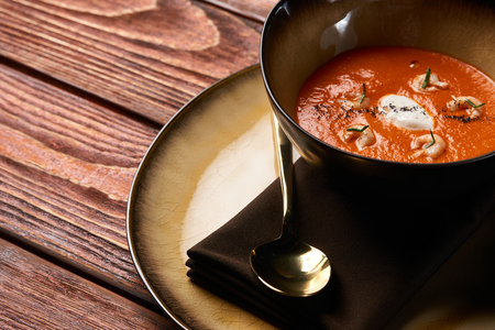 Hot Tomato soup with shrimp. Seafood creamy soup with goat cheese, olive powder, wild shrimps on bowl plate at wooden table, top view, close-up. Delicious vegetarian diet food.の写真素材