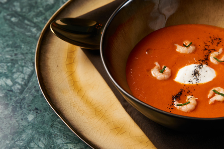 Hot Tomato soup with shrimp. Seafood creamy soup with goat cheese, olive powder, wild shrimps on...