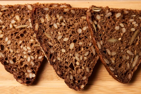 Slices of black rye bread. Three slices of fresh triangular rye bread with seeds on cutting board on...