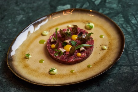 Beef tartare Steak with egg yolk, pistachios, truffle oil, green mayonnaise on porcelain plate. Classic tartare meat with ingredients. Luxury foodの写真素材