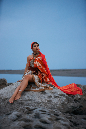 Summer fashionable girl portrait. Outdoor summer portrait of young pretty woman looking on sea, sitting on cliff. Travel conceptの写真素材