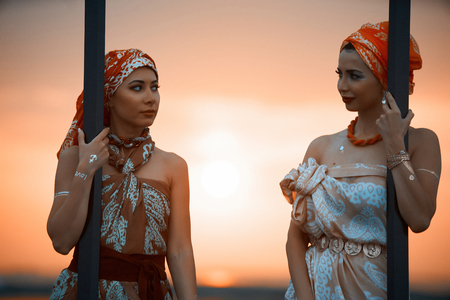 Girls traveler with wooden picture frame at colorful sea sunset.  Portrait of a Two Young women holding an empty frame.Summer vacation and travel concept.の写真素材