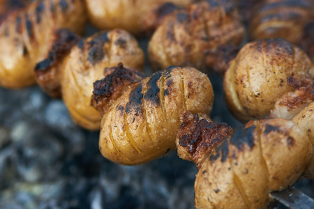 Baby potatoes grilled on skewers with lamb fat meat over coalsの写真素材