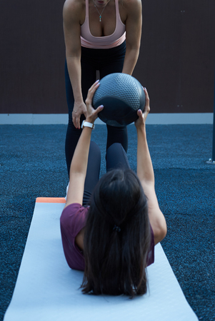 Fitness trainer helping young woman doing exercises with leather ball in gymの写真素材