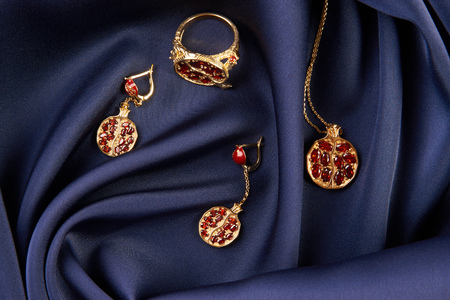 Rubies ring, necklace and earrings on blue silk background with copy space. Beautiful precious womens gold jewelry, close-up.の写真素材