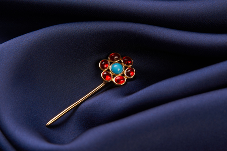 Gold hairpin with ruby precious stone on blue silk background with copy spce. Beautiful precious womens jewelry, close-upの写真素材