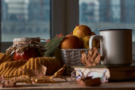 Autumn leaves, cup of coffee, warm scarf, fruits basket and book with glasses on the table. Old wooden table by the window in the autumn beautiful day, close-upの写真素材