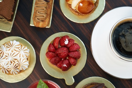 Breakfast time with cup of hot coffee and pieces of cream cake with strawberries and raspberries, sweets dessert breakfast snacks, close-up. Berry cupcakes dessert on wooden table background, top viewの写真素材