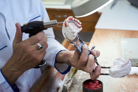 Dental technician working with articulator in dental laboratory, close-up. Dentist hands holds...