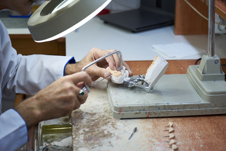 Dental technician working with articulator in dental laboratory, close-up. Dentist hands holds...