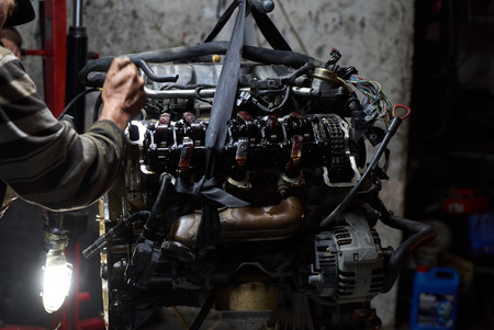 Car engine on crane hook in garage repair service, indoor, close-up.