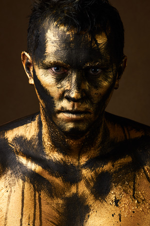 Hard Work Concept. Coal and Gold Miner, dirty worker against dark background. Man covered with gold paint and black crude oil color. Make-up and halloween theme.の写真素材