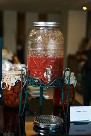 Tomato juice jar with tap. Fresh tomato juice in glass jar on Hotel restaurant table. Buffet catering service concept.の写真素材