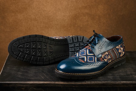 Ornamental elegant mens shoes on a dark wooden box, close-up. Mens business fashion concept. Blue color mens shoes over brown background with copy space.の写真素材