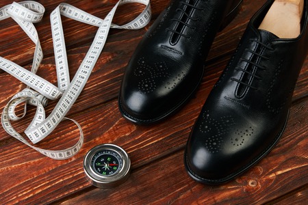Business travel concept with pair of black mens shoes, compass and measuring tape. Elegant mens leather shoes on a brown wooden table, close-upの写真素材