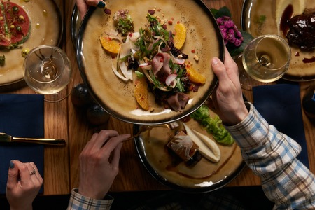 People friends eat healthy meals and drink alcohol at festive table served for party. Men and women friends having fun, celebrate with organic food on wooden table top view.の写真素材