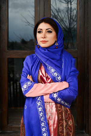 Beautiful azeri woman in traditional Azerbaijani dress standing at the wooden window outdoors....