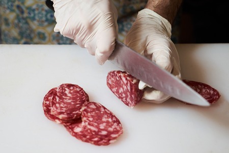 Mens hands cut sausage salami on a white cutting board, close-up.の写真素材