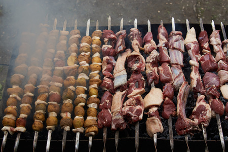 Preparation of shish kebab on skewers, close-up. Grilled shish kebab with vegetables. BBQ grill with...