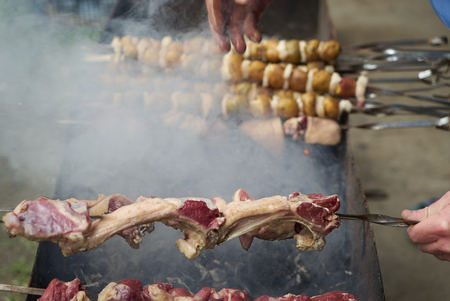 Preparation of shish kebab on skewers, close-up. Grilled shish kebab with vegetables. BBQ grill with lamb meat and potatoes. Barbecue time and weekend holidaysの写真素材