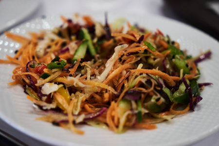 Mix vegetable salad on white dish, close-up. Healthy diet salad with fresh vegetables, red onion, cabbage, carrot, cucumberの写真素材